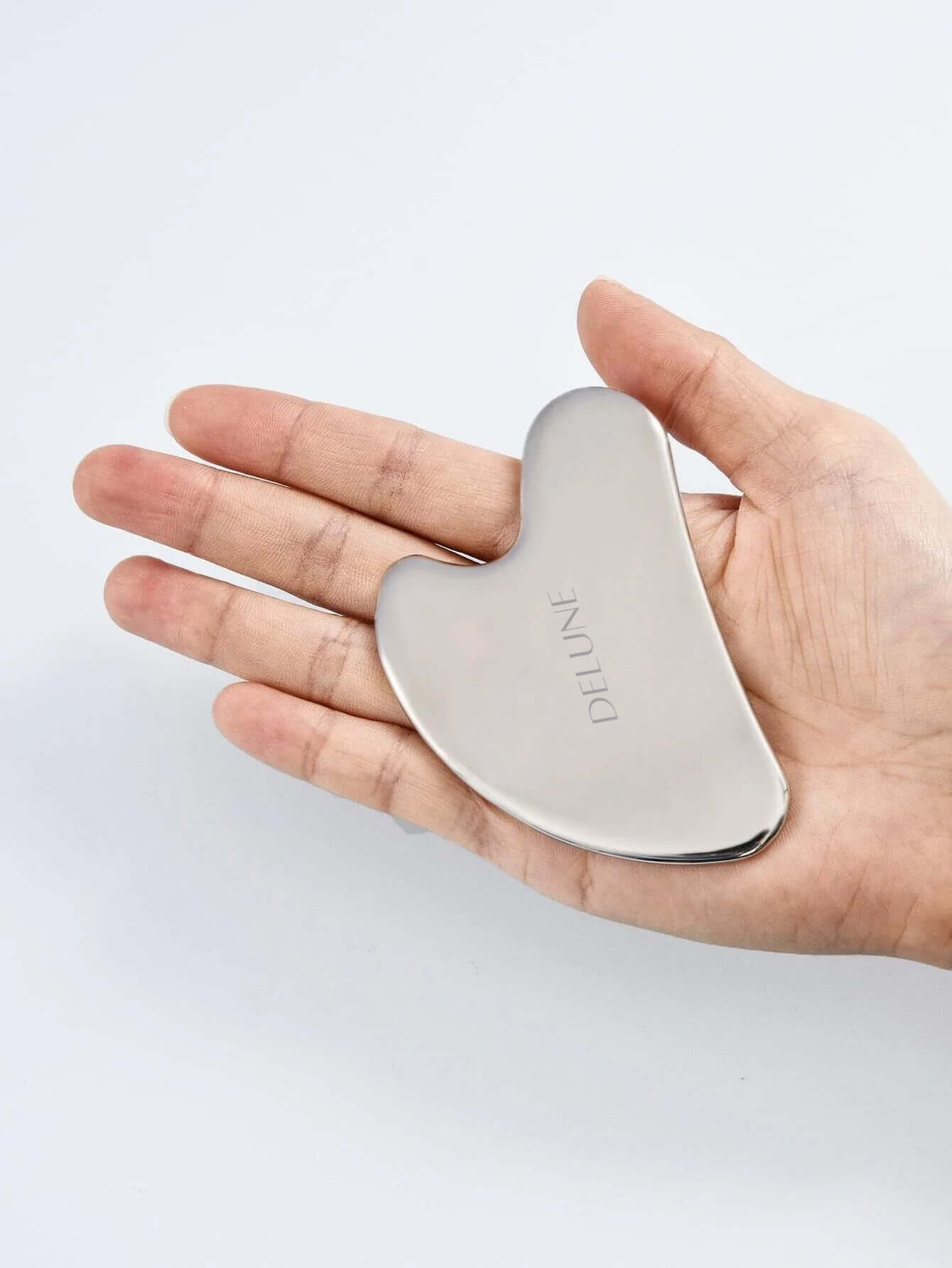 Stainless Steel Gua Sha tool held in hand, showcasing its smooth, contoured design for effective skincare and natural sculpting.