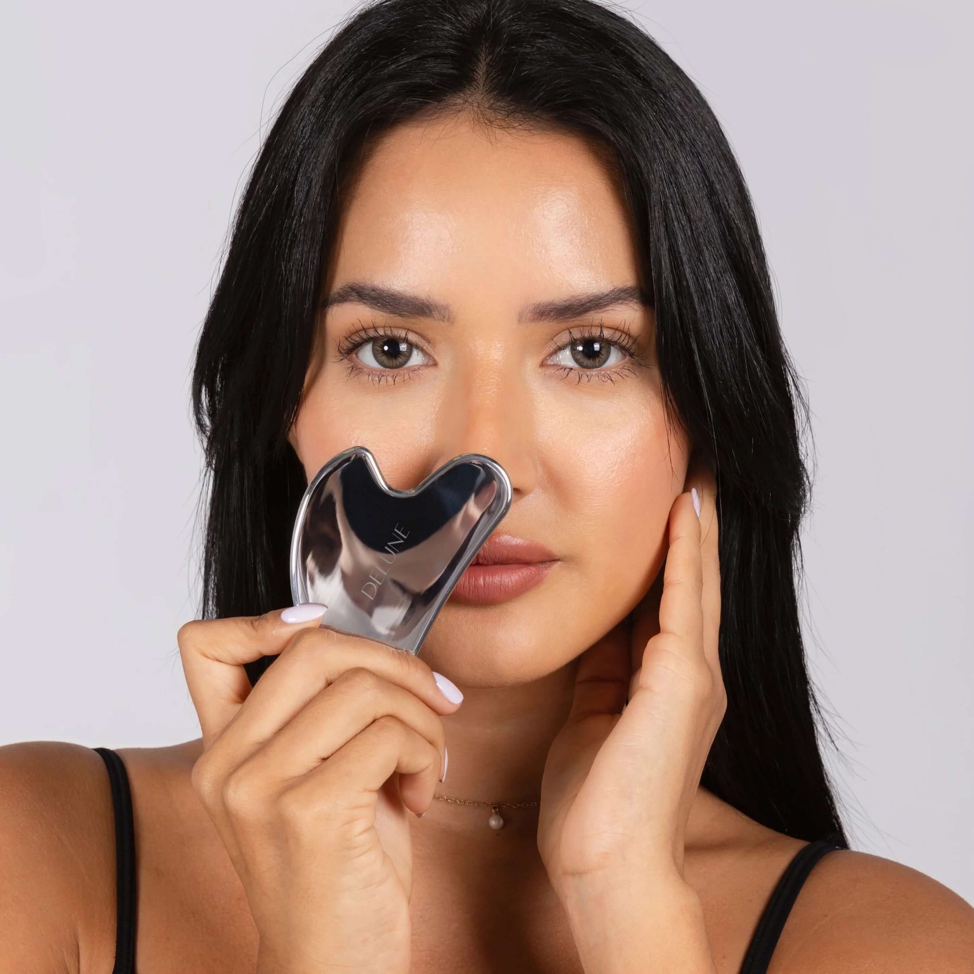 Woman using stainless steel Gua Sha for skincare contouring and beauty routine.