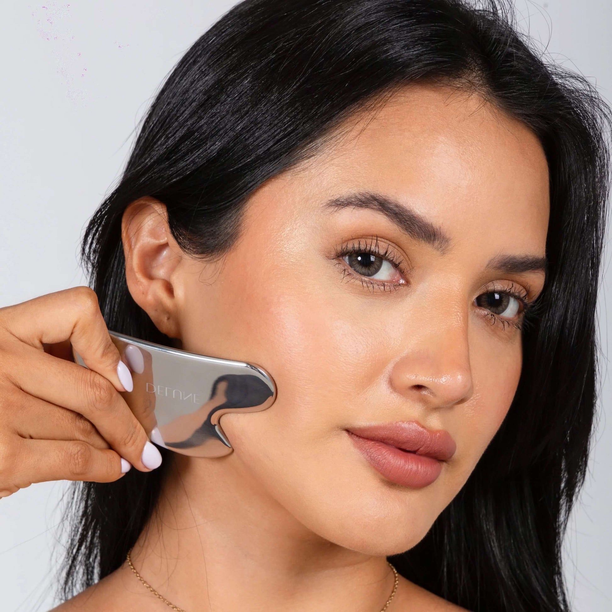 Woman using a stainless steel Gua Sha tool for natural contouring and youthful, radiant skin.