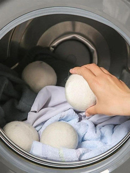 Hand placing organic wool dryer ball into drum with laundry, showcasing eco-friendly fabric softener alternative.