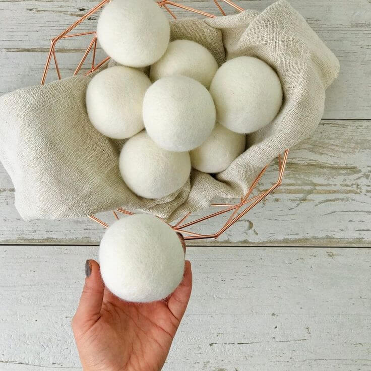 Hand holding organic wool laundry dryer ball, pack of 4 in a basket, eco-friendly fabric softener alternative for sensitive skin.