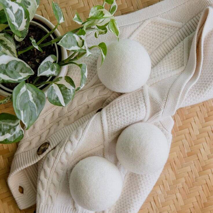 Set of 4 organic wool dryer balls on a knitted fabric with a potted plant beside, an eco-friendly fabric softener alternative.