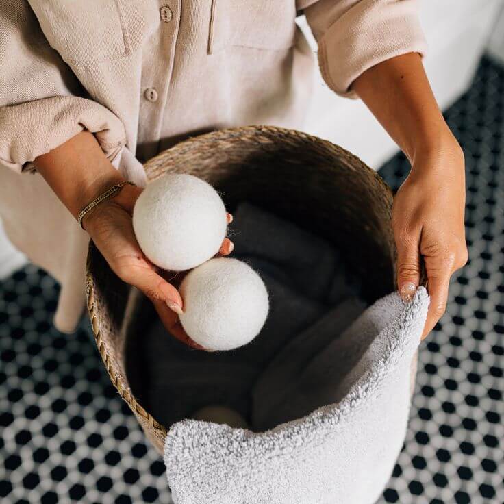 Woman holding organic wool dryer balls over a laundry basket, highlighting eco-friendly fabric softener alternative.