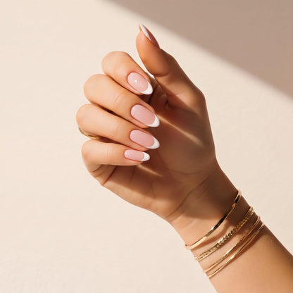 Hand wearing Delune French Manicure nail wraps with gold bangles against a warm plaster wall