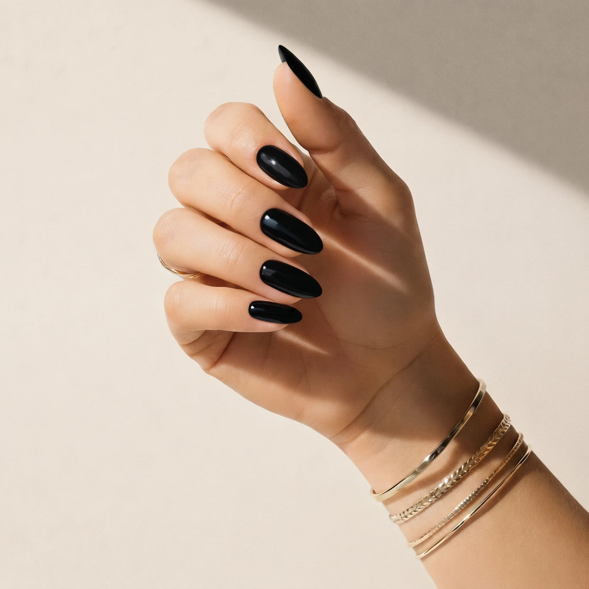 Hand wearing Delune Noir glossy black nail wraps with gold bangles against a warm plaster wall