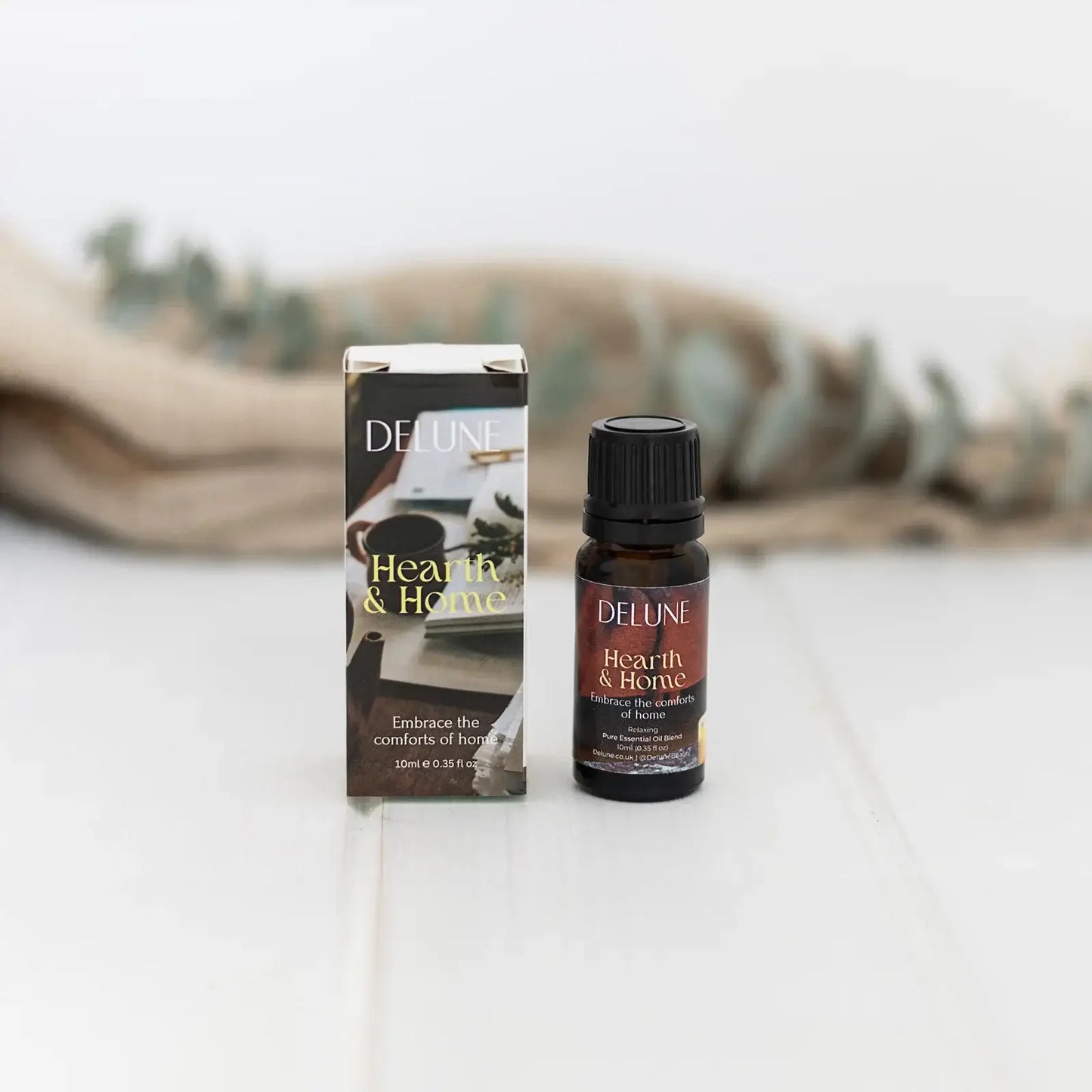 Hearth & Home Relax Wellbeing Blend essential oil bottle and box on a light surface, surrounded by soft greenery.